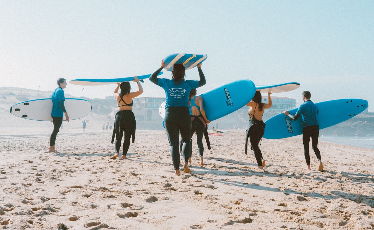 Group of surfers with blue surfboards heading to the ocean on a sunny beach.